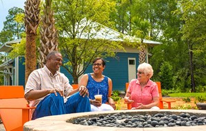 Three adults laughing around a fire pit