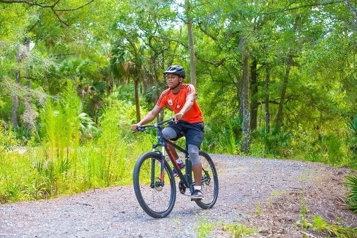 Boy on bike riding gravel trail through woods
