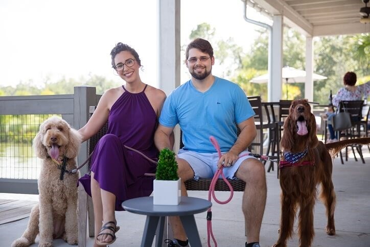 Young couple with two large dogs sitting on deck outside of Bexley clubhouse